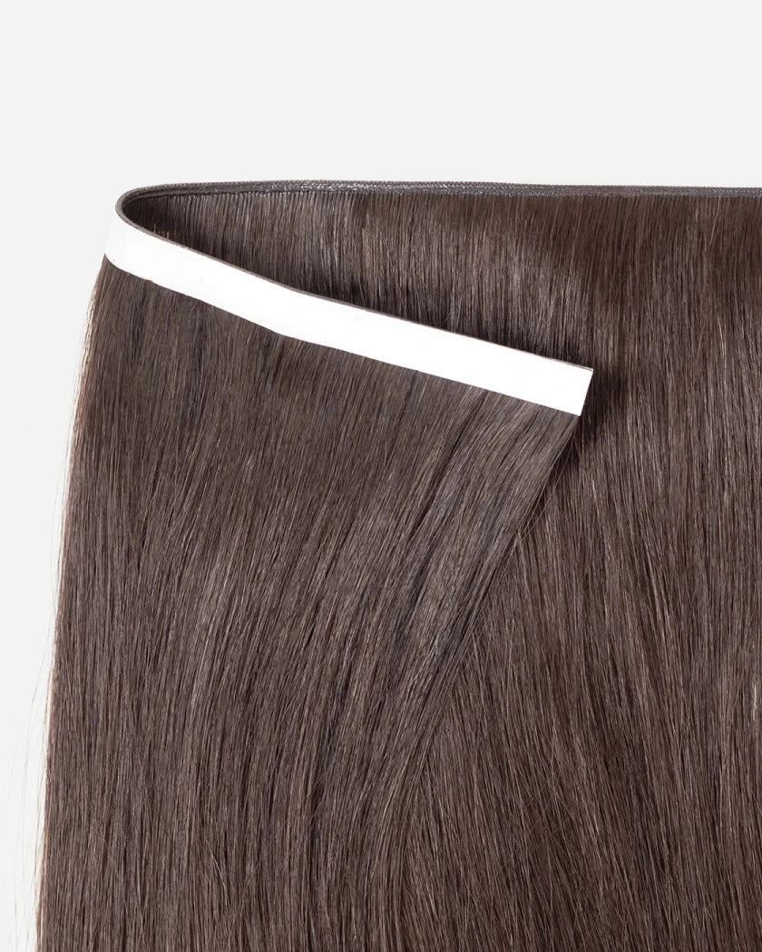 Brown hair extensions with a white tape on a light gray background