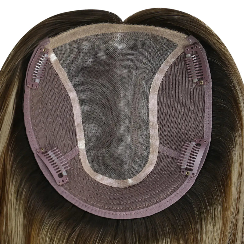 Load image into Gallery viewer, Close-up of the underside of a hairpiece extension, showing a semi-sheer mesh crown, brown adhesive base, and multiple metal hair clips holding the piece in place. The attached synthetic hair is light brown to blonde with subtle warm highlights.
