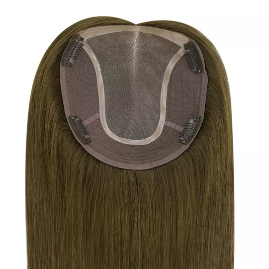 Close-up of the underside of a hairpiece extension, showing a semi-sheer mesh crown, brown adhesive base, and multiple metal hair clips holding the piece in place. The attached human hair is light brown to blonde with subtle warm highlights.