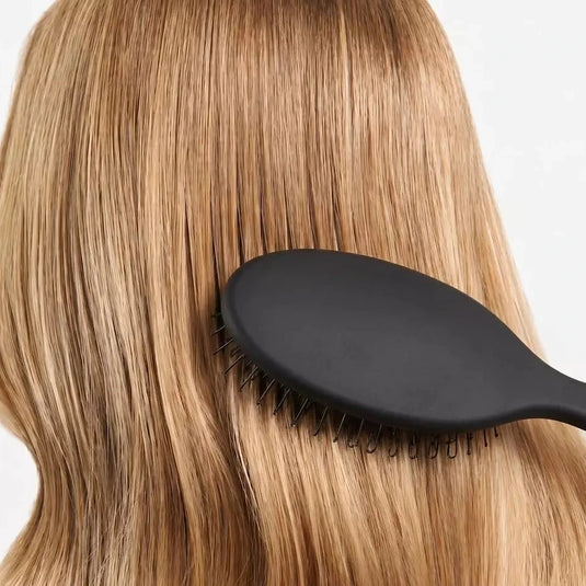 Black hairbrush being used on blonde hair against a white background