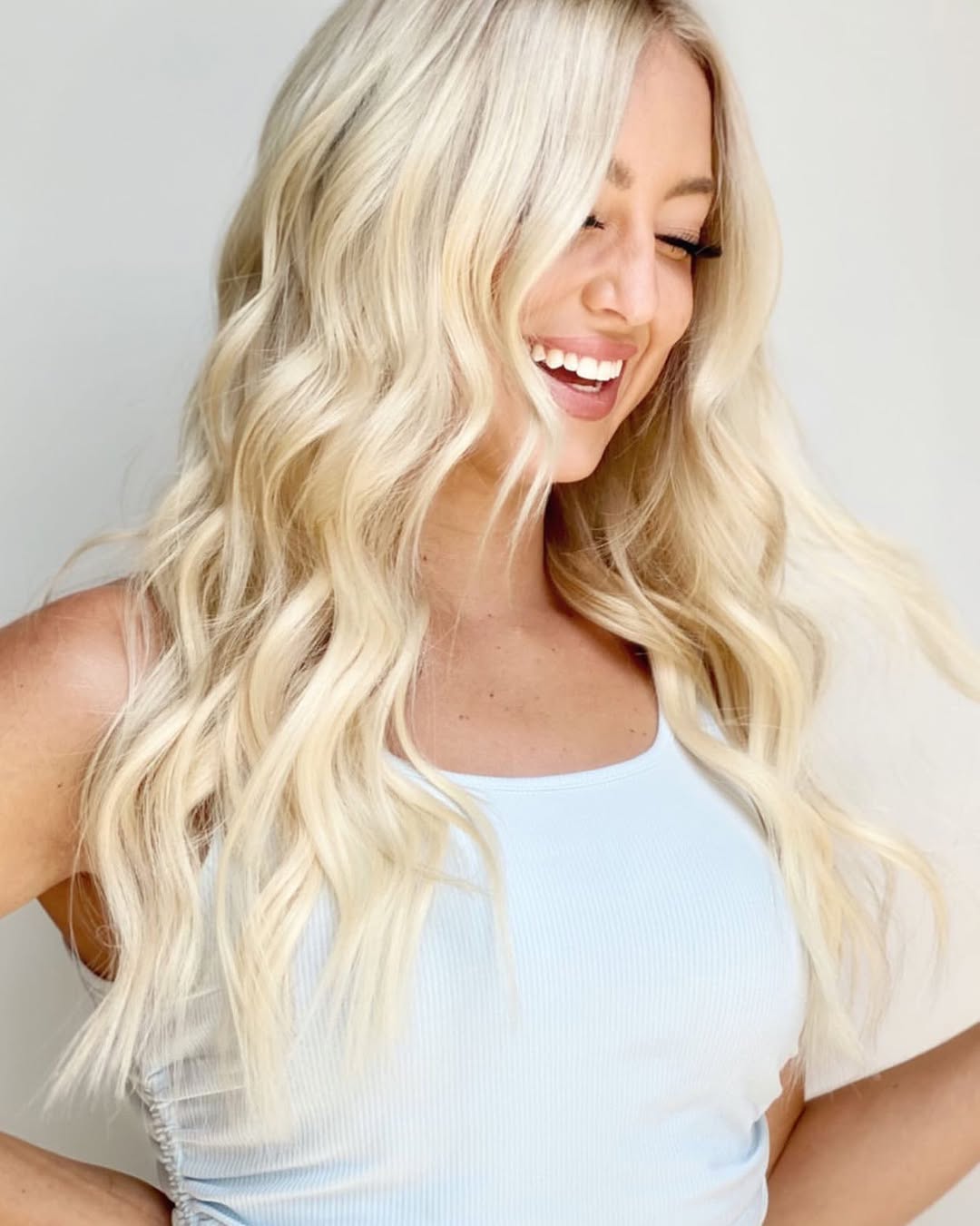 Woman with long, wavy blonde hair smiling against a plain background