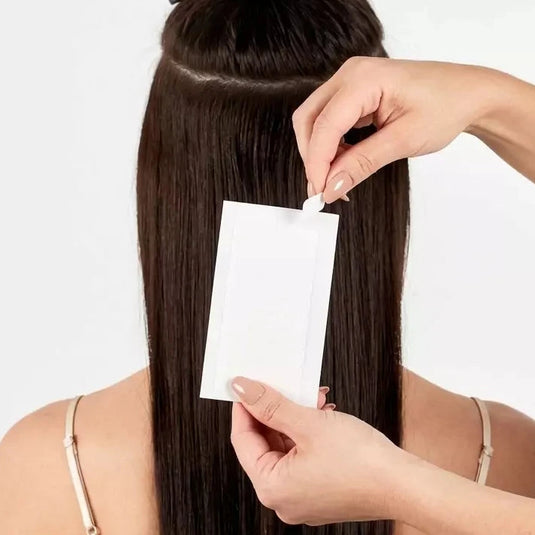 Person applying a white strip to their hair against a plain background