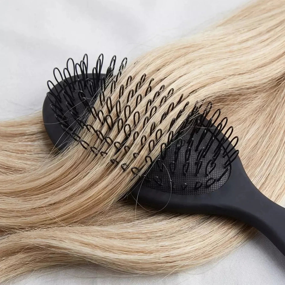 Black hairbrush with bristles on a blonde hair strand against a light background