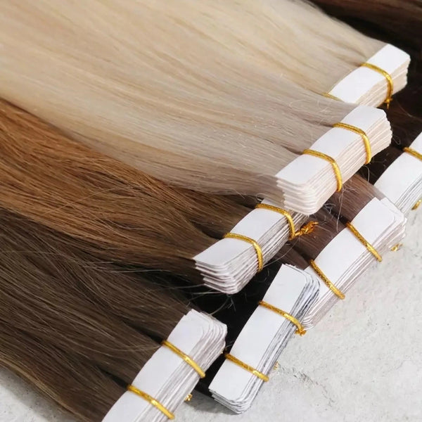 Bundles of tape hair extensions with visible color gradient on a neutral background