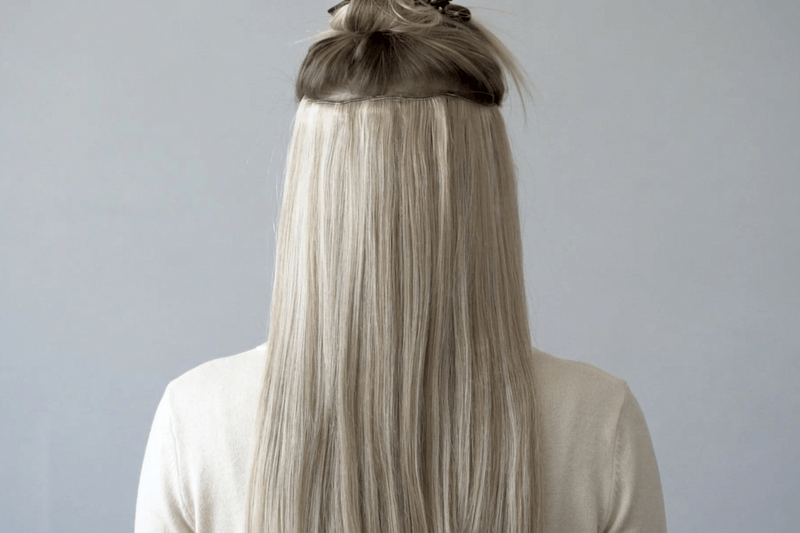 Person with long blonde hair styled in a half-up, half-down style against a gray background