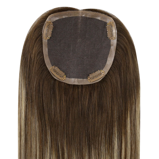 A straight hair piece with a center part, featuring light brown and blonde highlights, attached to a dark brown mesh cap with gold metal clips.