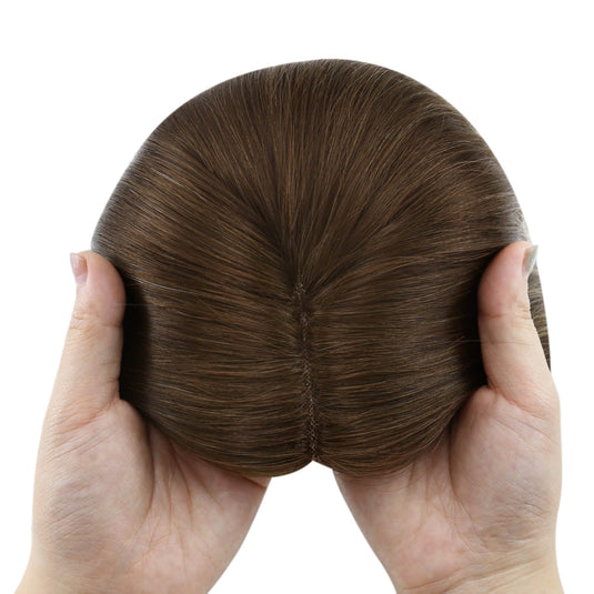 A brown hairpiece held up by two hands against a plain white background.