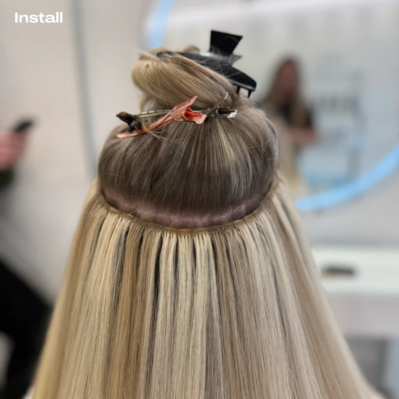 Load image into Gallery viewer, Close-up of machine weft hair extension being styled with a blurred salon background
