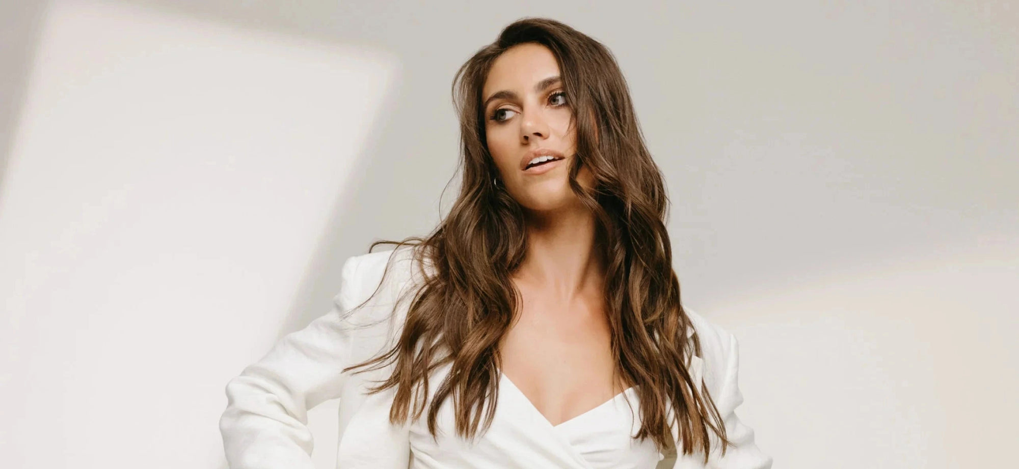 Woman wearing a white top and jacket against a plain background