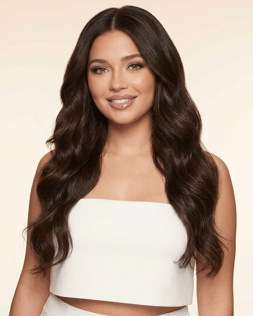 Woman with long, wavy hair wearing a white strapless top against a beige background
