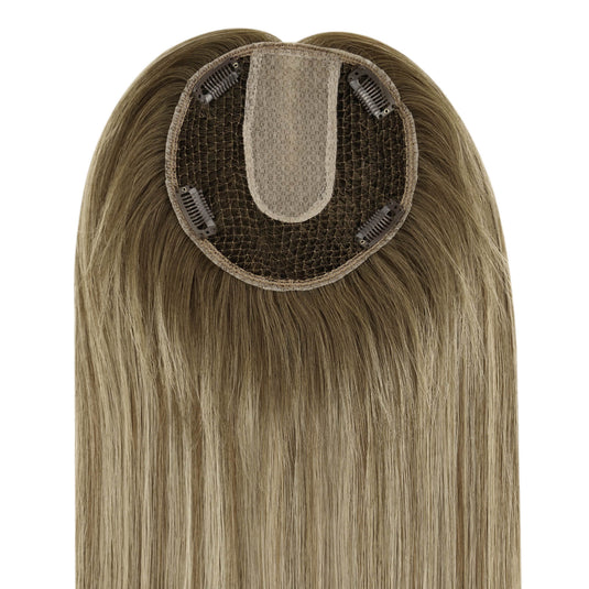 A close-up of a straight hairpiece section, showing the beige adhesive base and dark mesh with clip-in springs, on a plain white background.