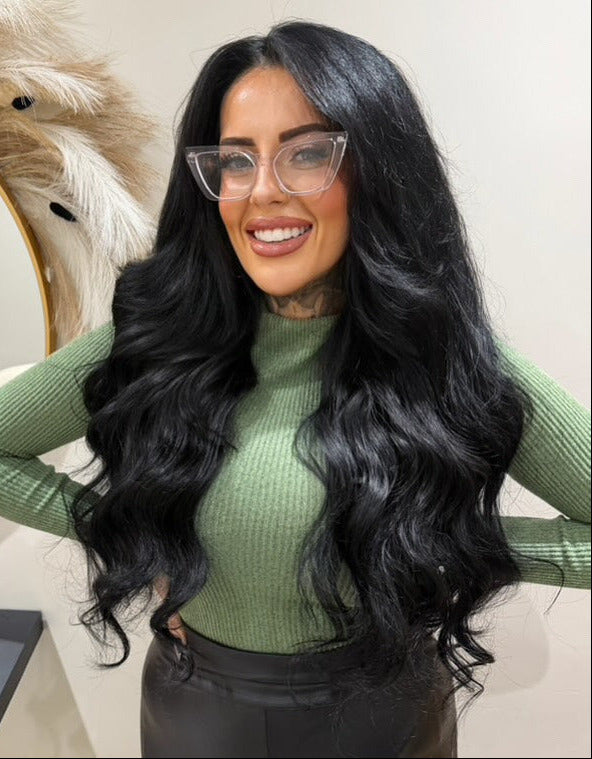 Woman with long black hair wearing glasses and a green sweater in an indoor setting