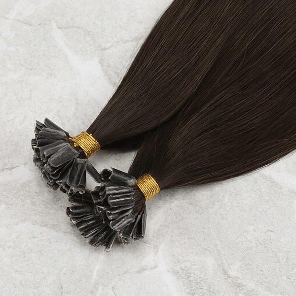 Two bundles of dark brown hair extension tips with black adhesive and gold bands, displayed on a light gray textured surface.