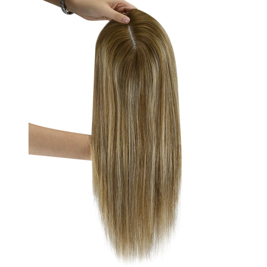 A long hairtopper with a warm golden-brown and light blonde ombré color, held up by a hand against a plain white background.