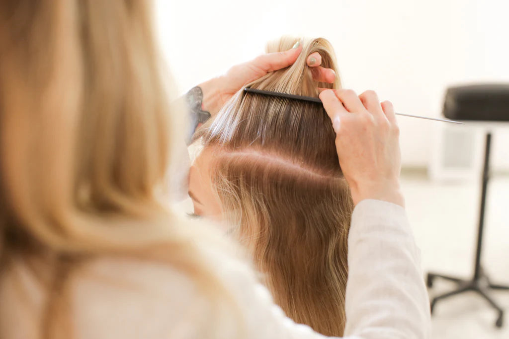 A model getting a hair extension fitted by a hairstylist in a salon setting.