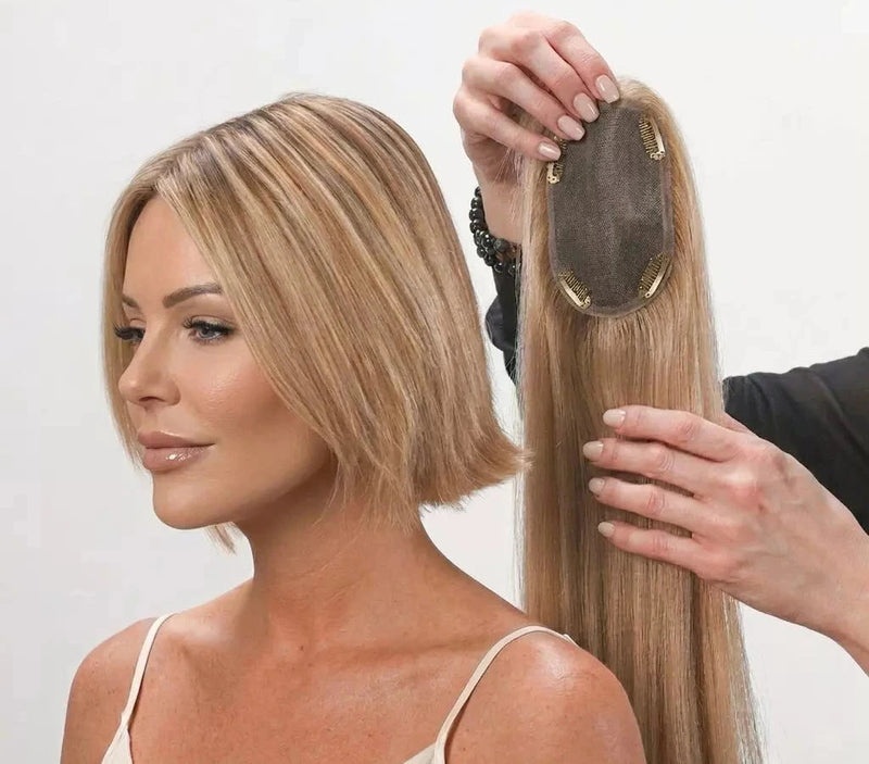 Woman with a blonde hair topper being held by a hand against a white background
