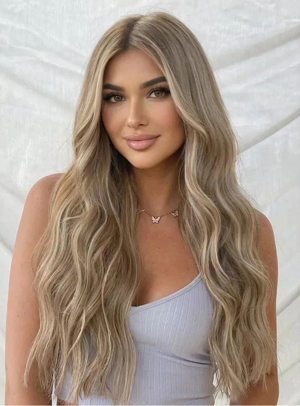 Woman with long, wavy blonde hair wearing a light blue top against a textured white background