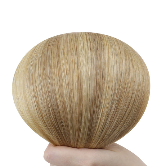 Blonde hair extensions held by a hand on a white background