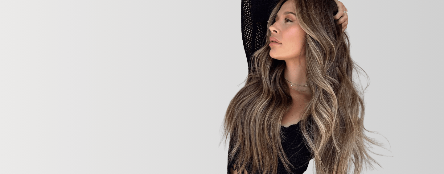 Woman with long, wavy hair styled in a side part against a plain background