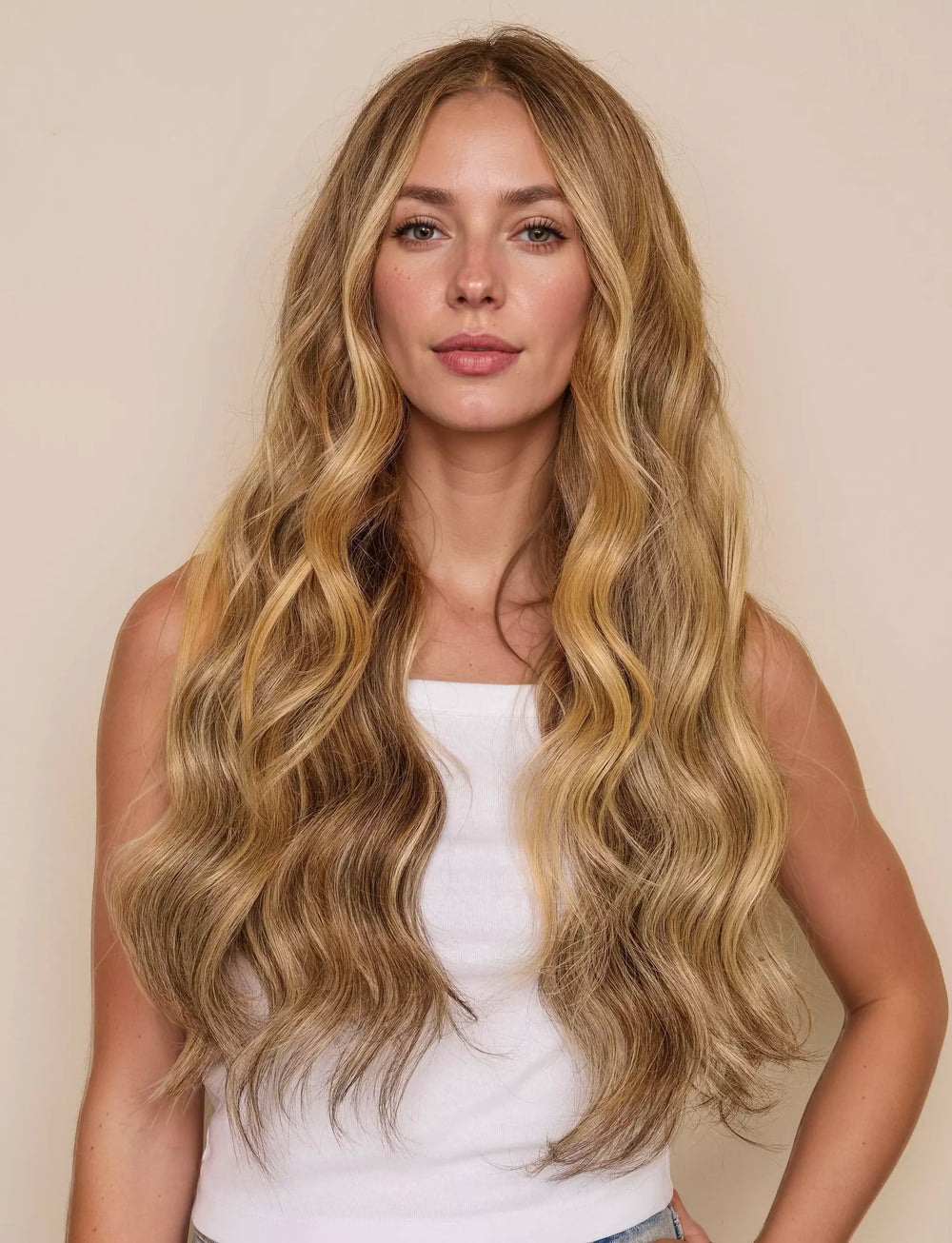 Woman with long, wavy blonde hair wearing a white top against a beige background