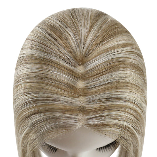 A close-up of a topper on a mannequin head, showing a center part with blended light brown and blonde streaks against a plain white background.