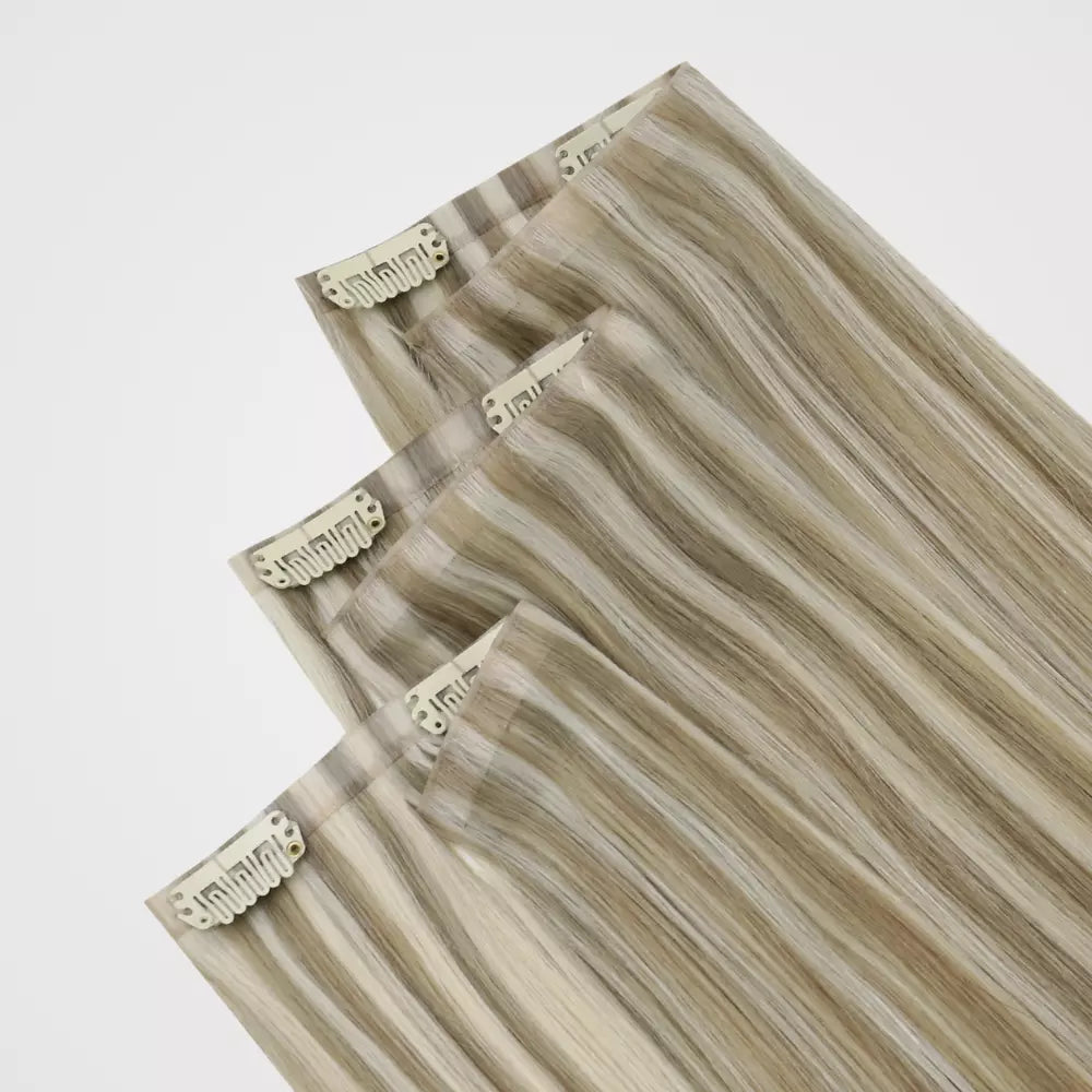 Three hair clip-in extensions with a wavy, layered pattern in beige, brown, and blonde tones, shown against a plain light gray background.