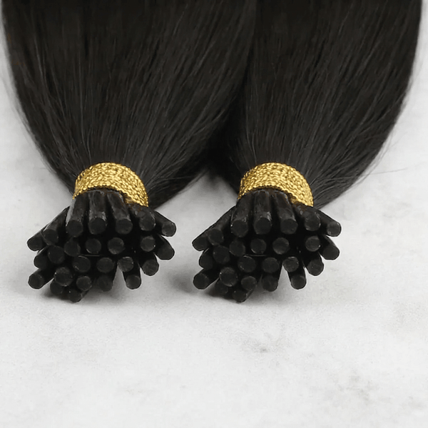 Two bundles of black hair extension tips with gold metallic bands, displayed on a light gray marble surface.