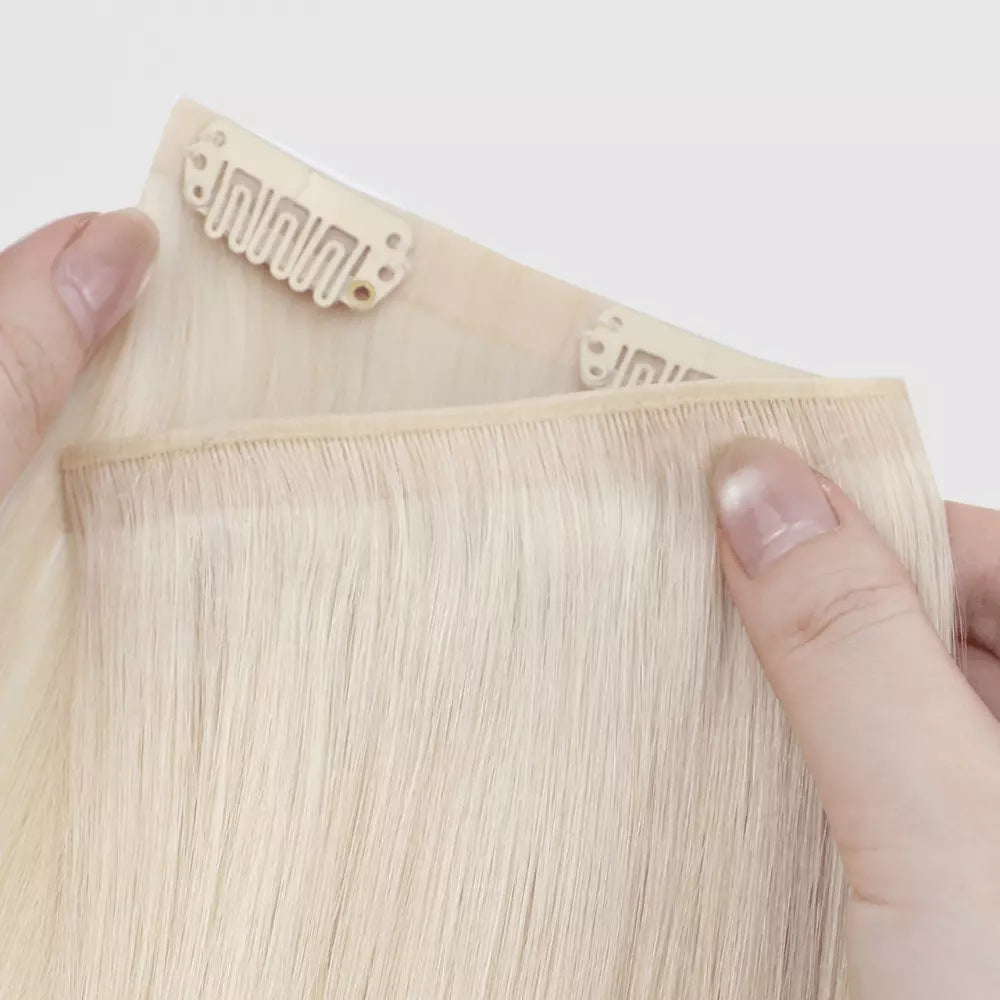 Blonde genius clip in hair extensions held by a hand with a clear background