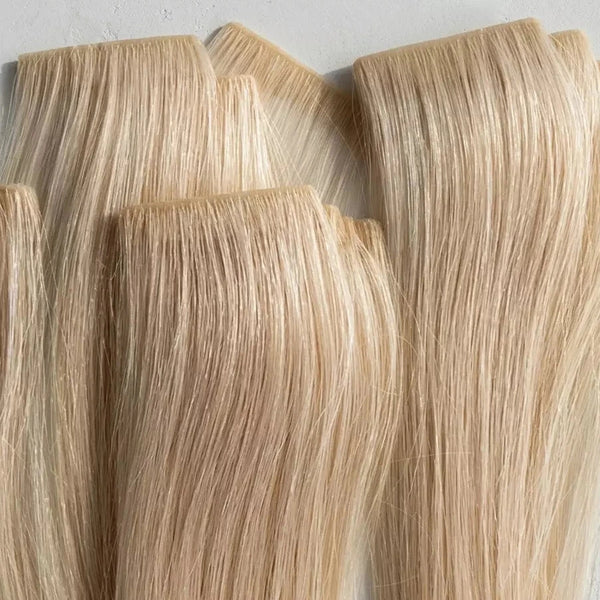 Blonde tape in hair extensions on a light gray background