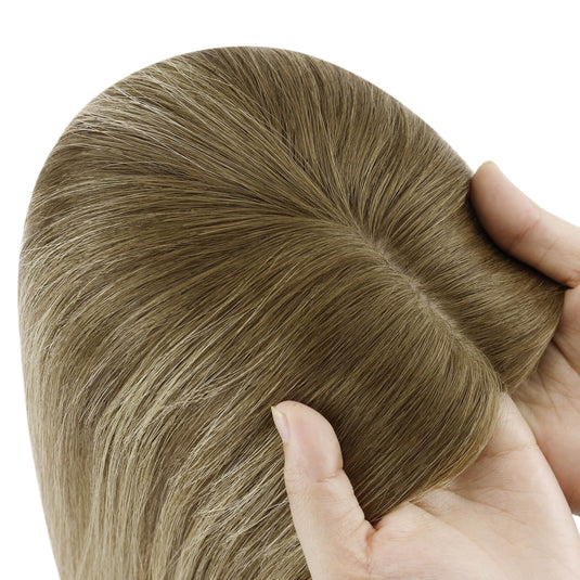 A close-up of a brown hair topper section held by hands against a plain white background, showing the texture and color of the hair.